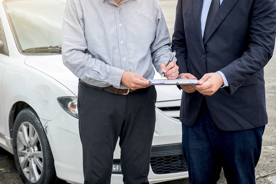Insurance Agent Examine Damaged Car And Customer Filing Signature